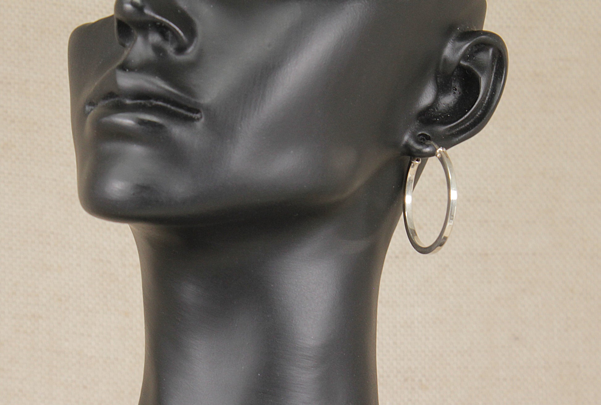 A sterling silver hoop earring displayed on a black mannequin head against a light beige background.