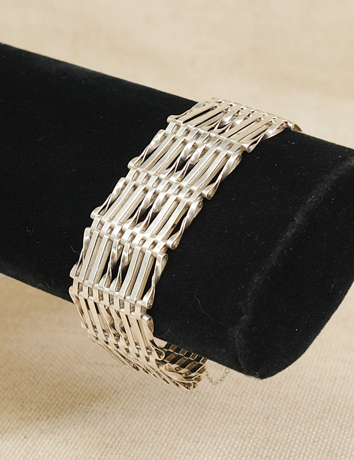 A sterling silver gate link bracelet displayed on a black cylindrical jewelry stand against a light beige fabric background.