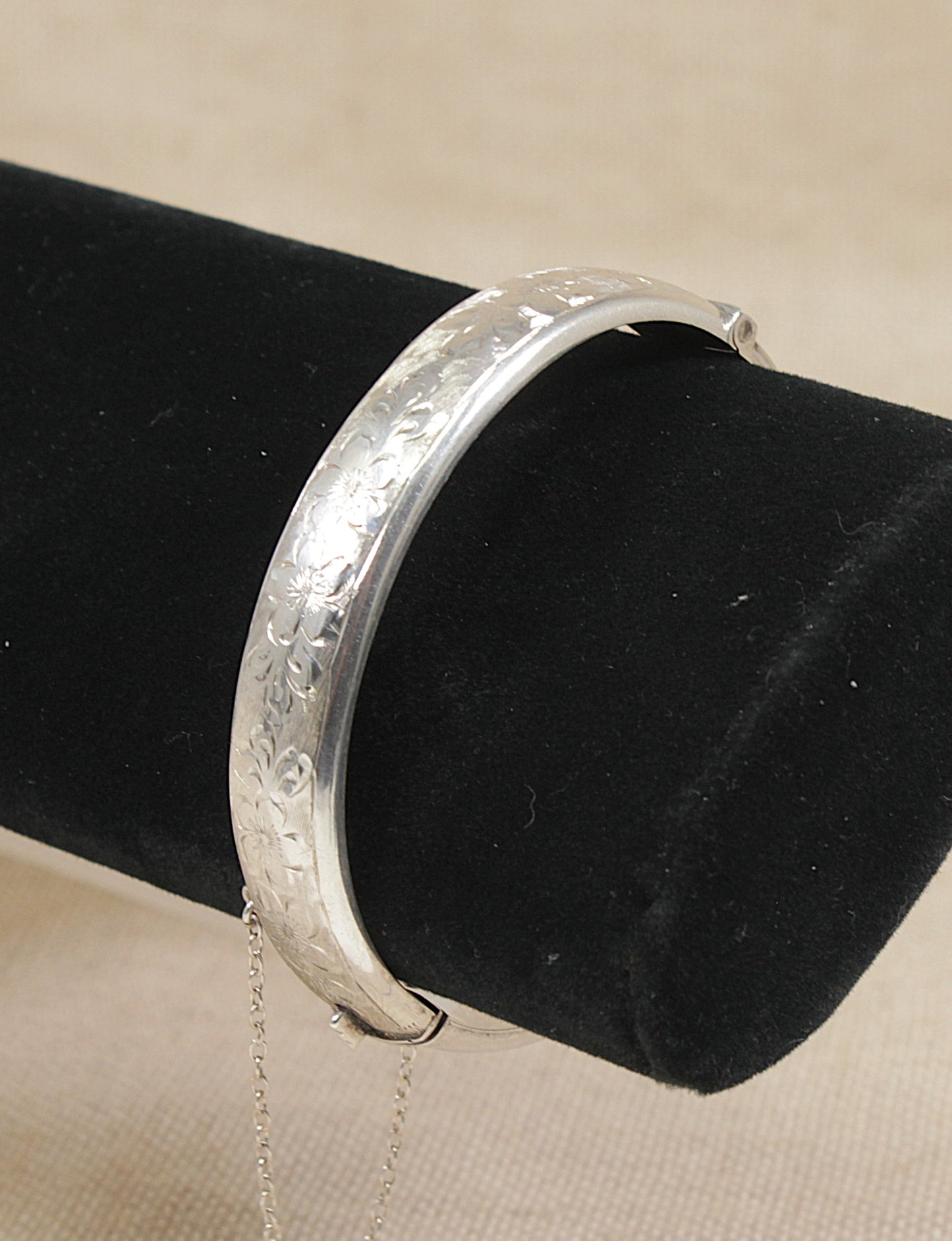 Vintage silver cuff bangle bracelet on a black velvet stand against a beige background