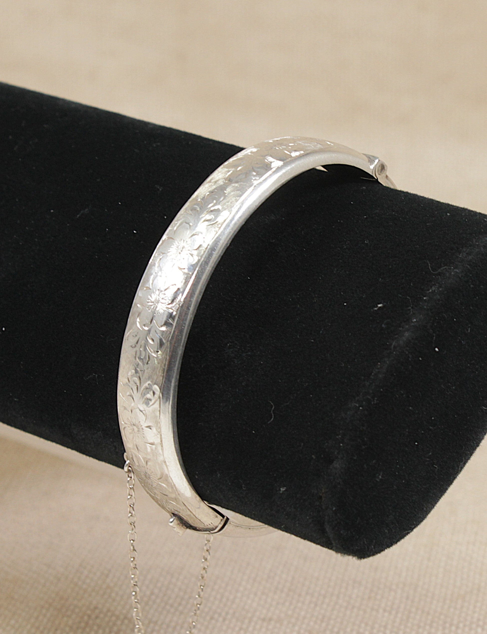 Vintage silver cuff bangle bracelet on a black velvet stand against a beige background