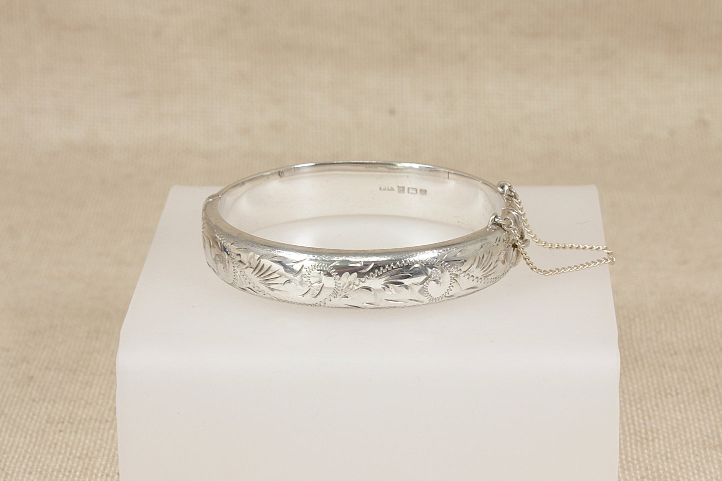 Vintage 1970's Silver hinged bangle bracelet with floral designs on a white cube against a beige background