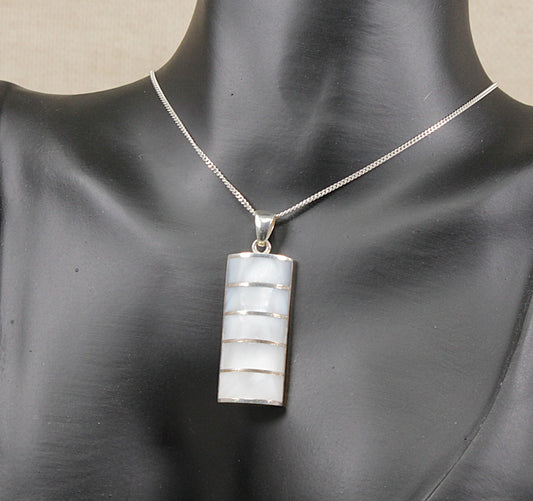A silver chain necklace with a rectangular pendant featuring horizontal bands of white mother-of-pearl, displayed on a black mannequin bust.
