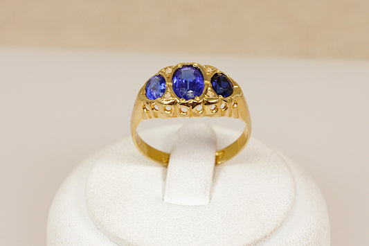 Edwardian antique gold ring with three blue gemstones on a white stand against a beige background