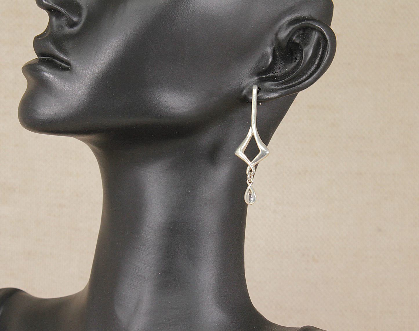 A silver and topaz geometric dangle earring by kit heath displayed on a black mannequin head against a light beige background.