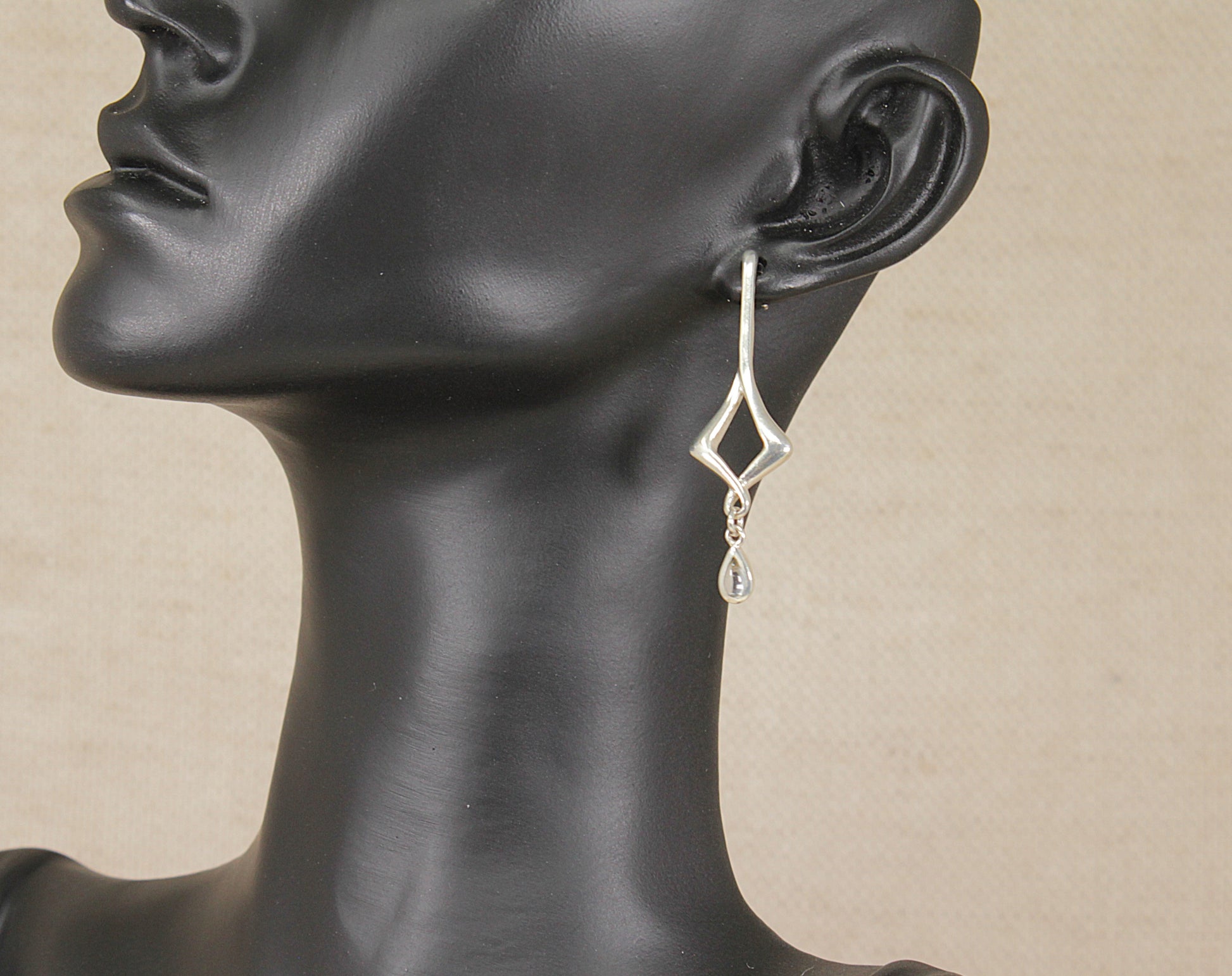 A silver and topaz geometric dangle earring by kit heath displayed on a black mannequin head against a light beige background.
