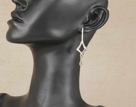 A silver and topaz geometric dangle earring by kit heath displayed on a black mannequin head against a light beige background.