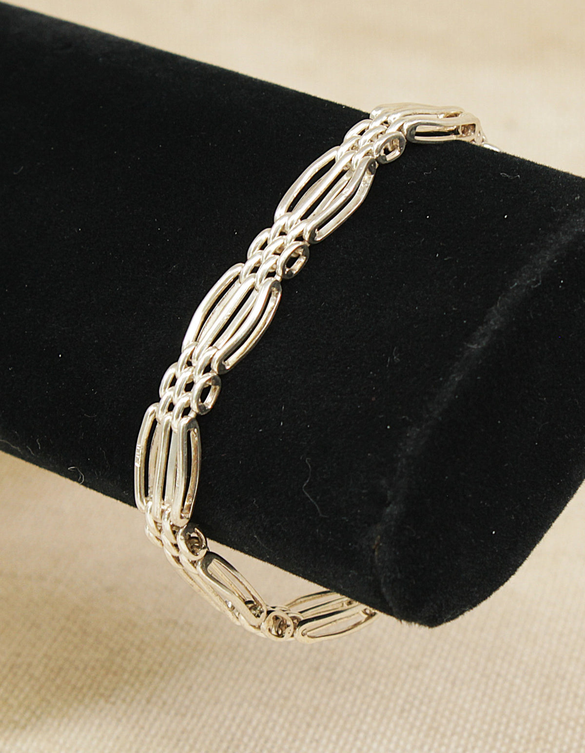 A sterling silver link bracelet displayed on a black velvet jewelry stand against a light beige fabric background.