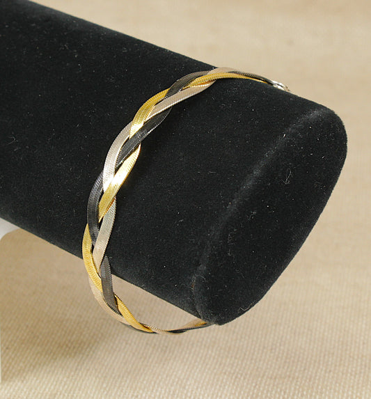A plaited sterling silver bracelet in gold, silver, and black tones, displayed on a black velvet jewelry stand against a beige fabric background.