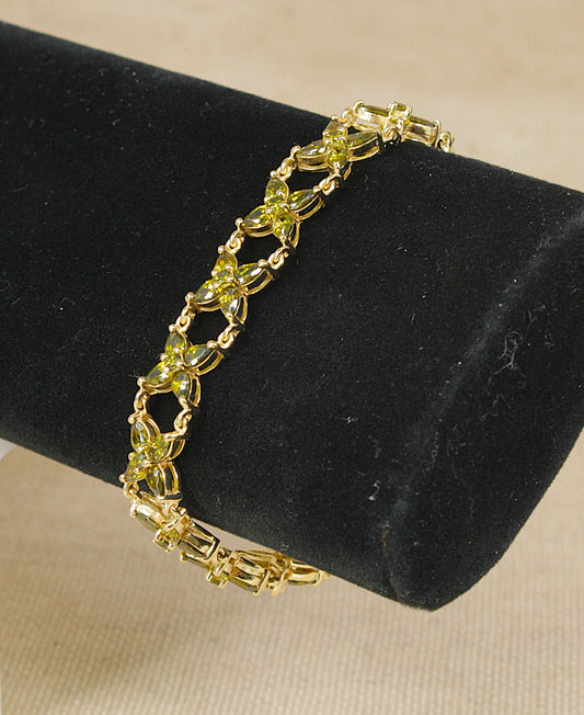 A gold-tone sterling silver bracelet with green marquise-cut crystals, displayed on a black velvet jewelry stand against a beige fabric background.