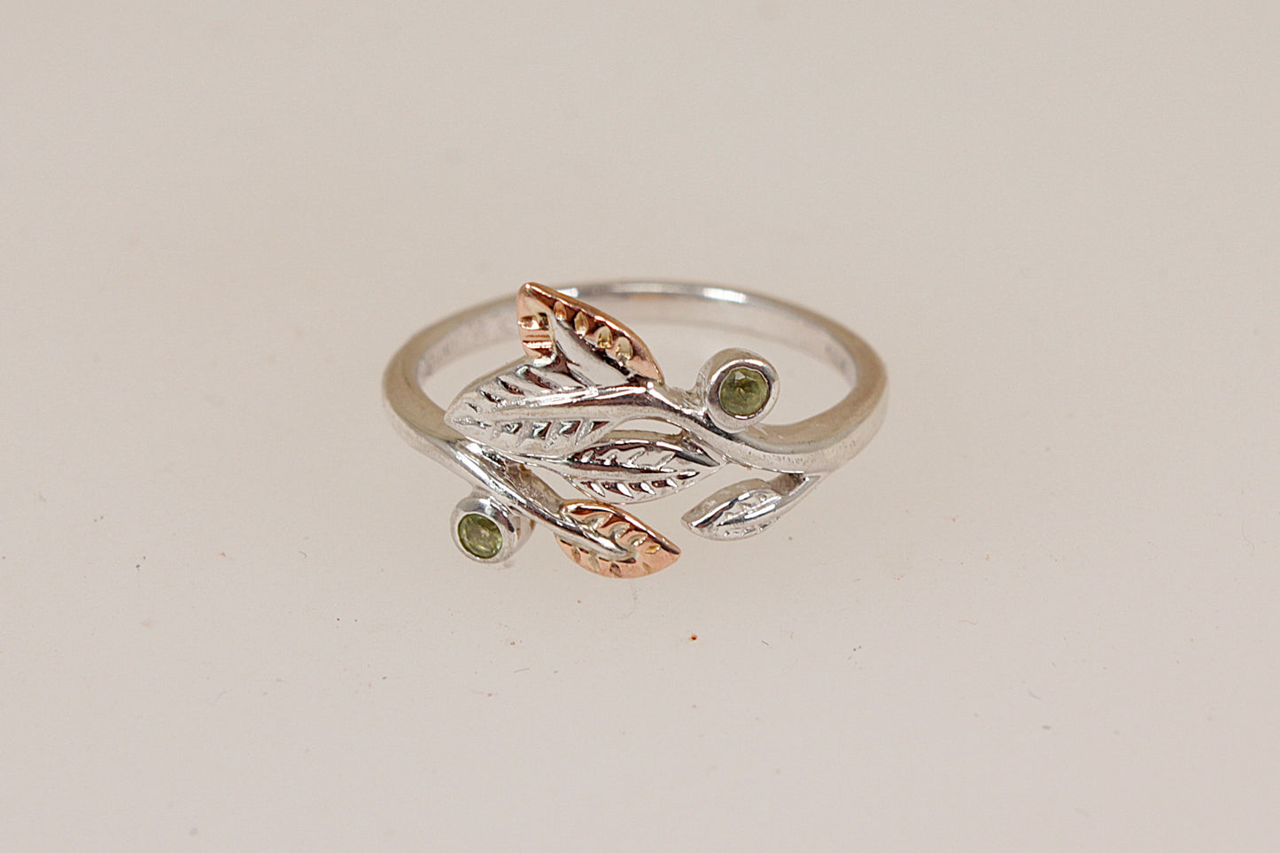 A two-tone silver and welsh gold ring by Clogau featuring a leafy branch design with small gemstone accents, set against a plain light beige background.