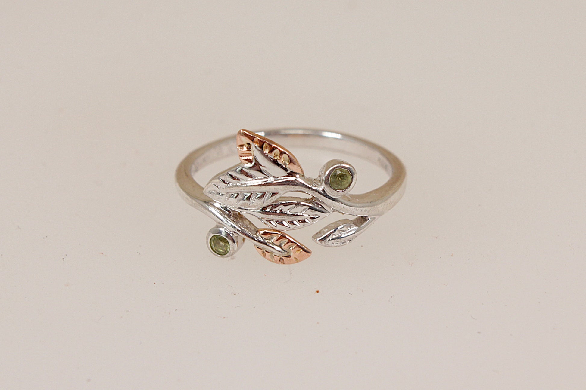 A two-tone silver and welsh gold ring by Clogau featuring a leafy branch design with small gemstone accents, set against a plain light beige background.