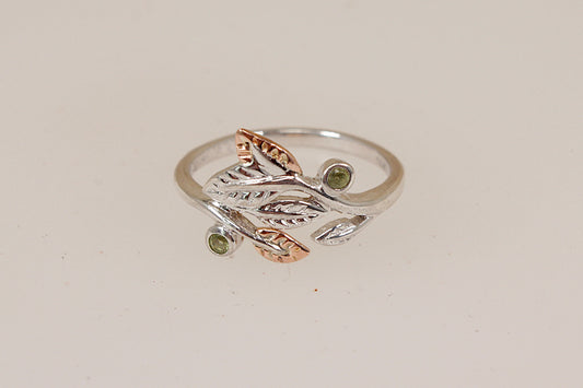 A two-tone silver and welsh gold ring by Clogau featuring a leafy branch design with small gemstone accents, set against a plain light beige background.