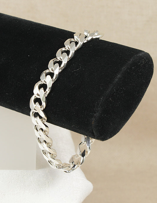 Silver flat curb link chain bracelet on a black velvet stand with a beige background