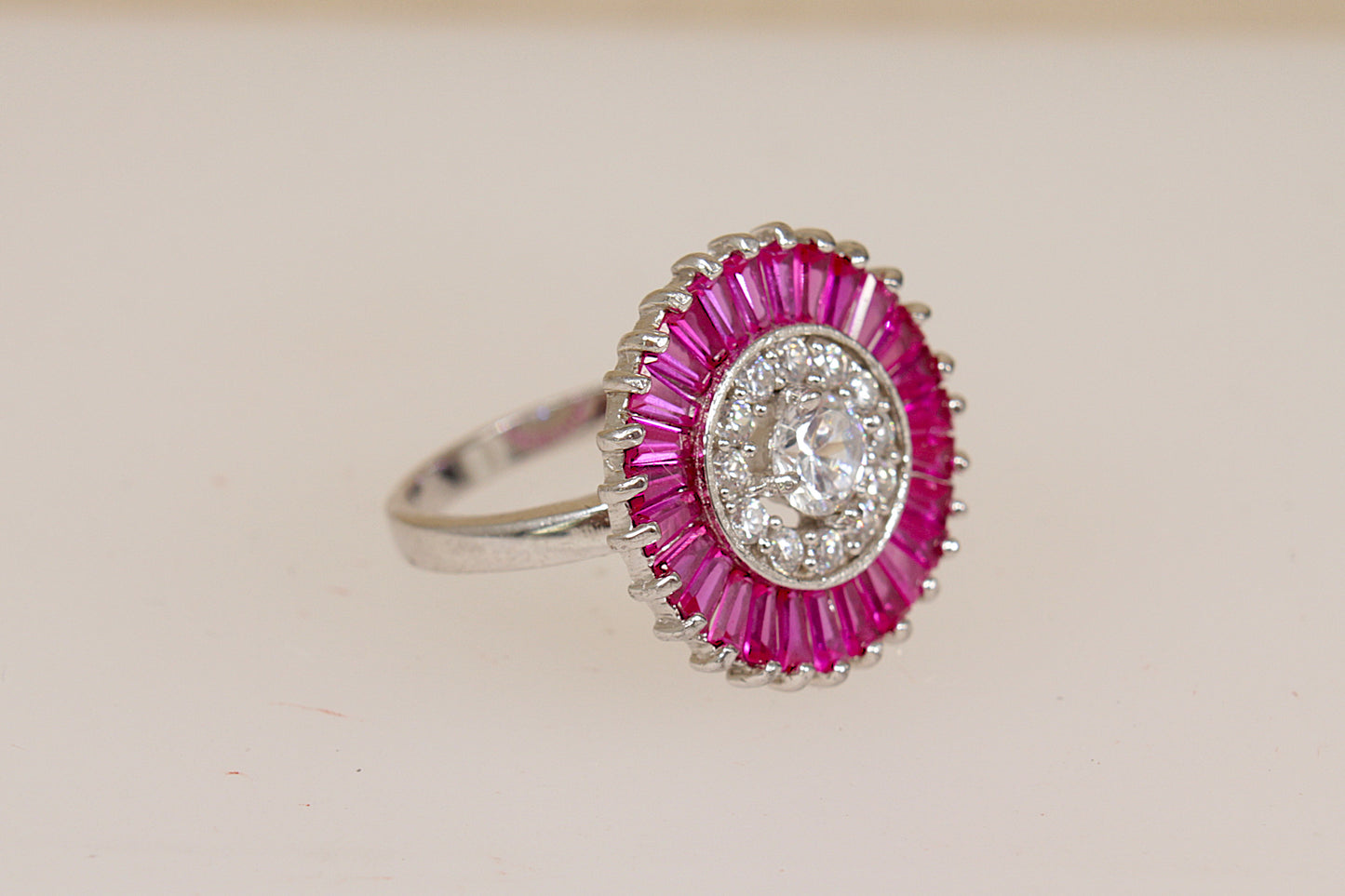A close-up of a sterling silver ruby and white crystal ring with a central clear gemstone and a surrounding halo of pink ruby stones.