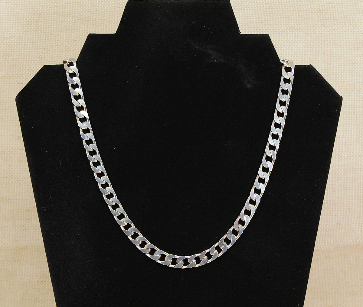 A silver Flat Curb link chain necklace displayed on a black velvet jewelry bust against a light beige textured background.