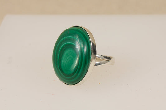 A silver ring featuring a large, oval-shaped cabochon green malachite pattern gemstone, set against a plain light background.