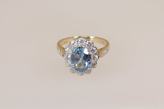 Gold ring with a blue topaz gemstone and cz diamond simulant gemstone accents on a light beige background