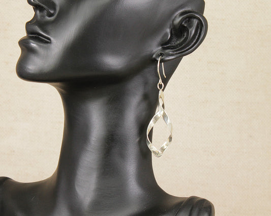 Silver swirl drop earring on a black mannequin head against a beige background