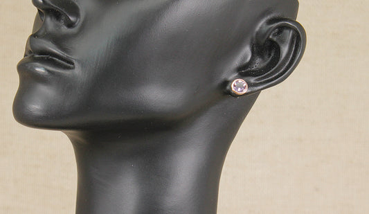 A close-up of a black mannequin head and neck wearing a small round Clogau silver amethyst and gold stud earring on a beige background.