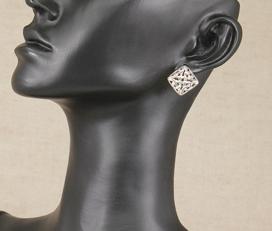 A silver geometric filigree stud earring displayed on a black mannequin head against a neutral beige background.