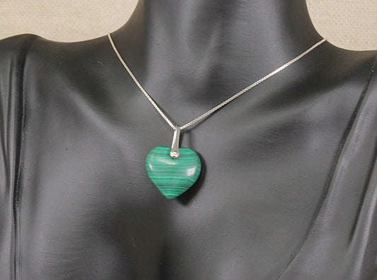 A heart-shaped green malachite pendant necklace on a silver chain, displayed on a black mannequin bust.