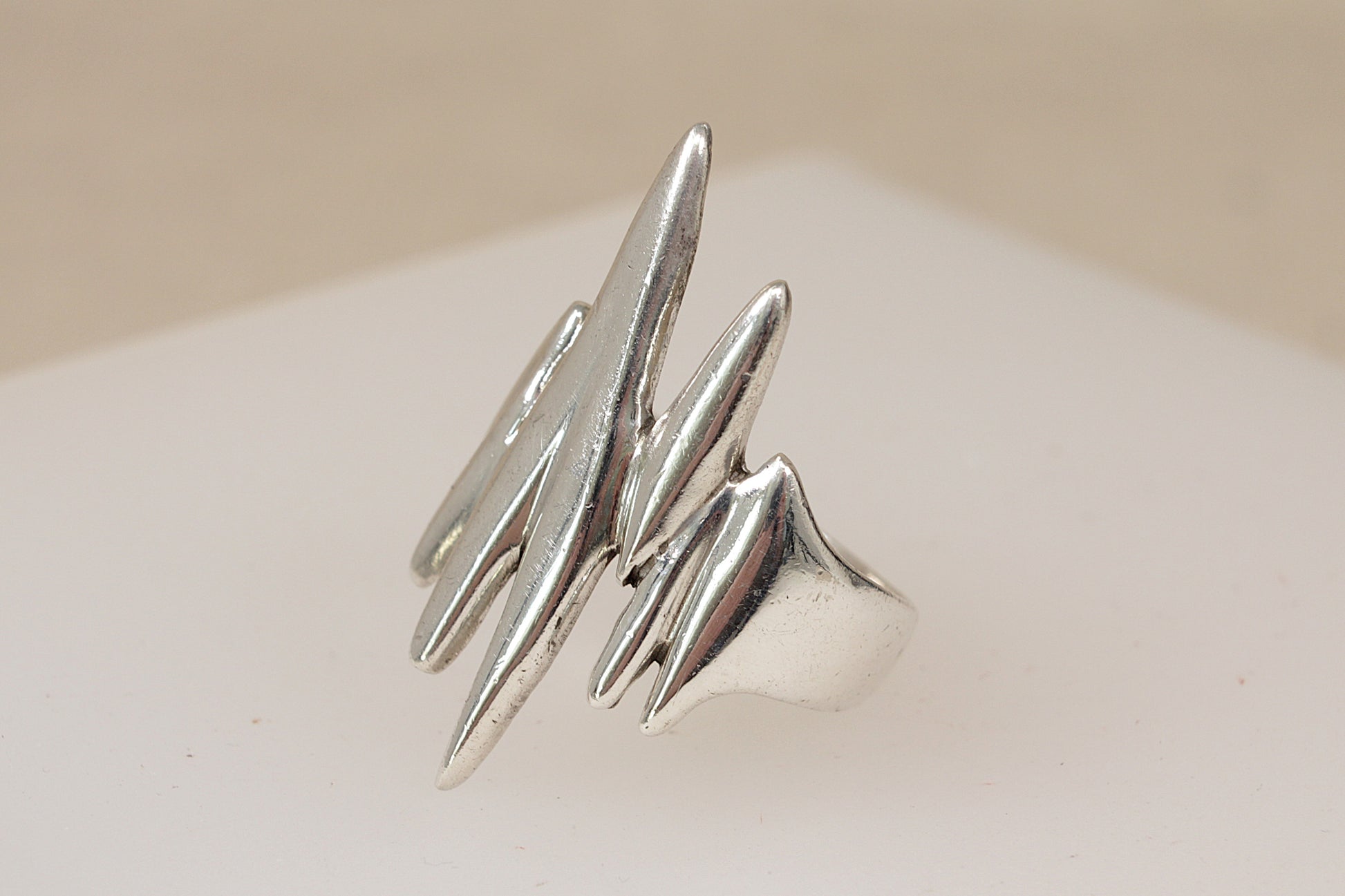 A rare vintage danish brutalist modernist silver ring with multiple abstract, jagged prongs, displayed on a neutral beige surface.