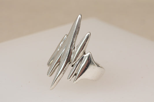A rare vintage danish brutalist modernist silver ring with multiple abstract, jagged prongs, displayed on a neutral beige surface.