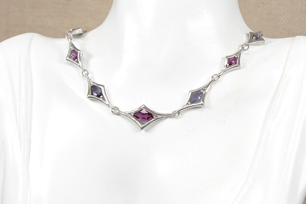 A sterling silver Art Deco style necklace displayed on a white mannequin bust. The necklace features five diamond-shaped links, each set with a faceted amethyst and iolite gemstone.