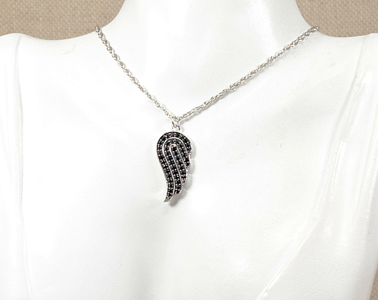 A silver angels wing shaped pendant necklace with black stones, displayed on a white mannequin bust.