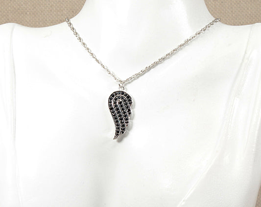 A silver angels wing shaped pendant necklace with black stones, displayed on a white mannequin bust.