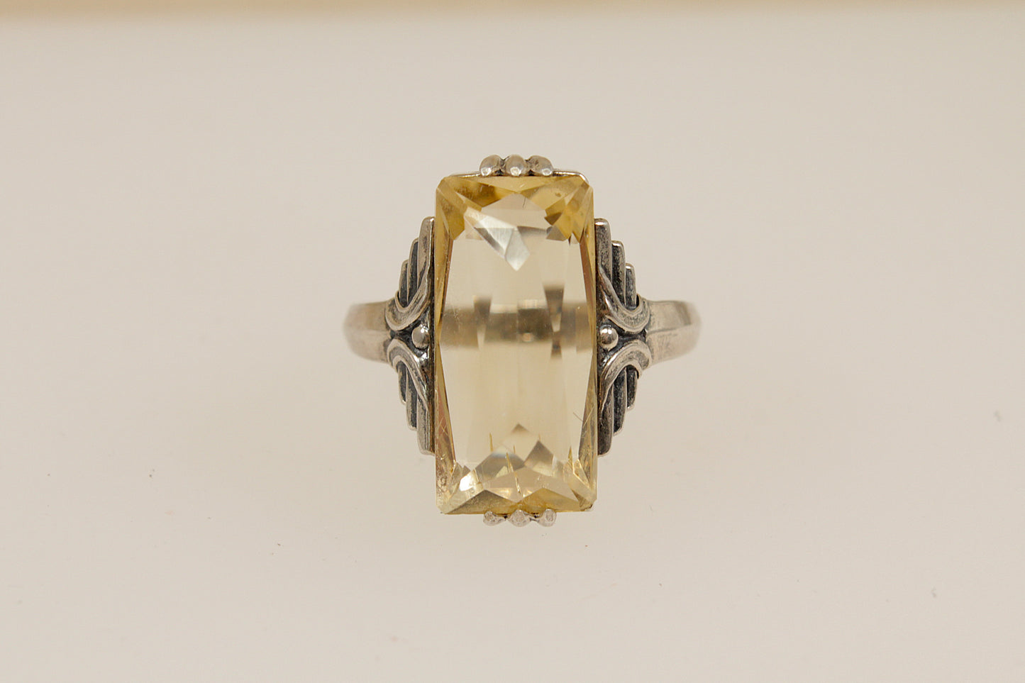 Art Deco Silver Ring with a large yellow citrine gemstone and intricate silver band on a beige background