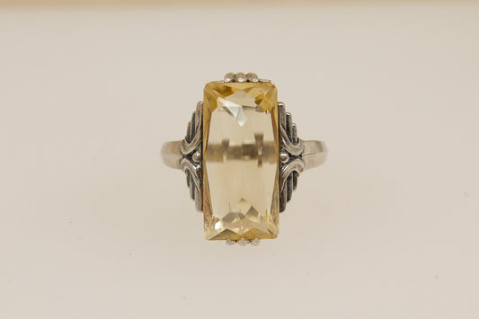 Art Deco Silver Ring with a large yellow citrine gemstone and intricate silver band on a beige background