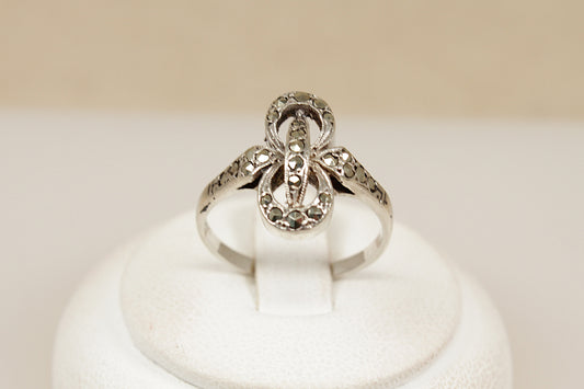 Silver ring with intricate marcasite gemstone design on a white stand against a beige background