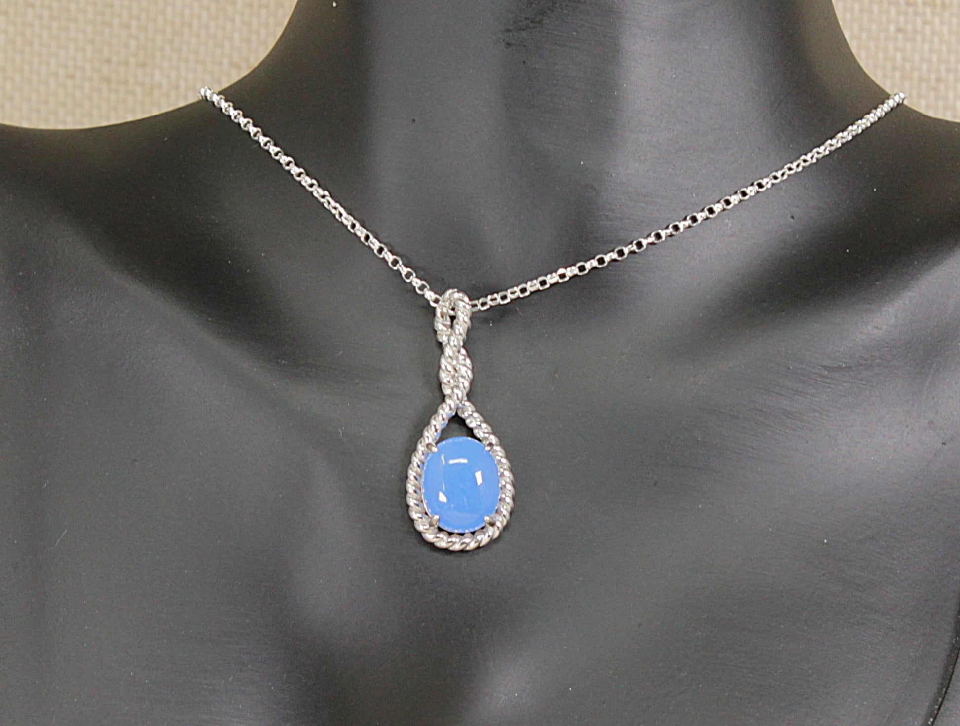 A silver pendant necklace with a teardrop-shaped blue cabochon stone, displayed on a black mannequin bust.