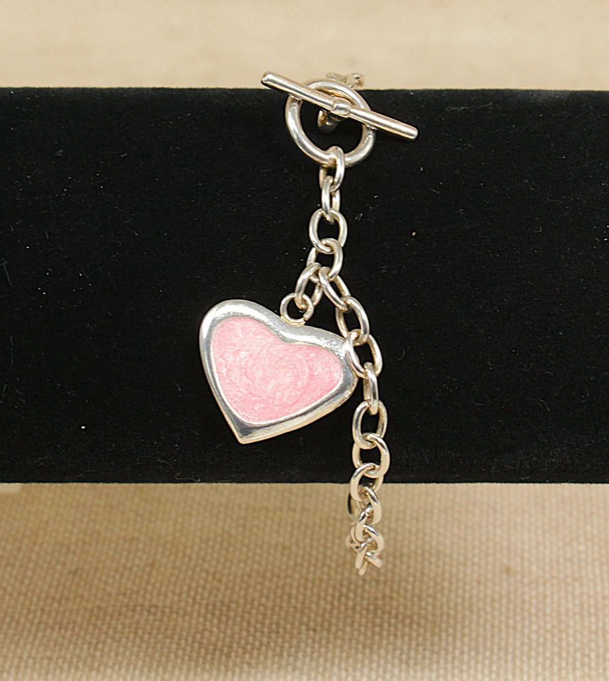 Heart-shaped pink charm on a silver belcher chain bracelet against a black background