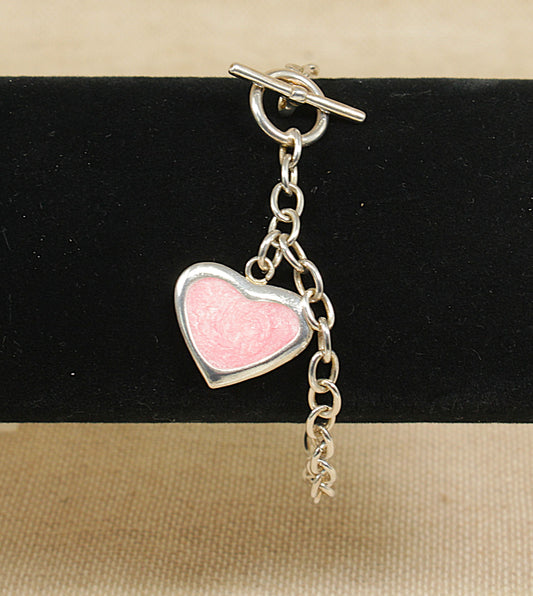 Heart-shaped pink charm on a silver belcher chain bracelet against a black background