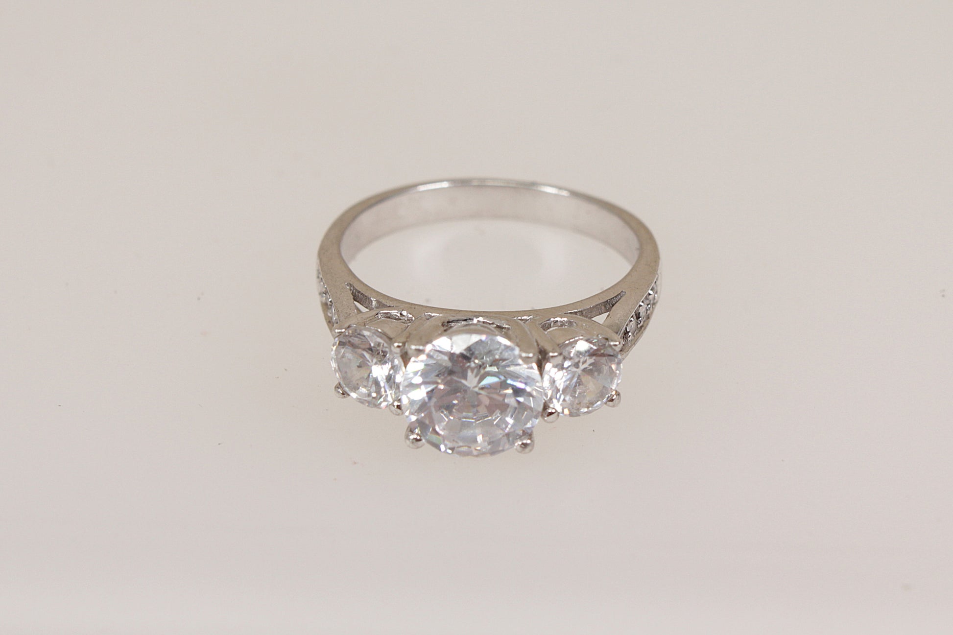 Silver ring with three clear cubic zirconia gemstones on a light gray background