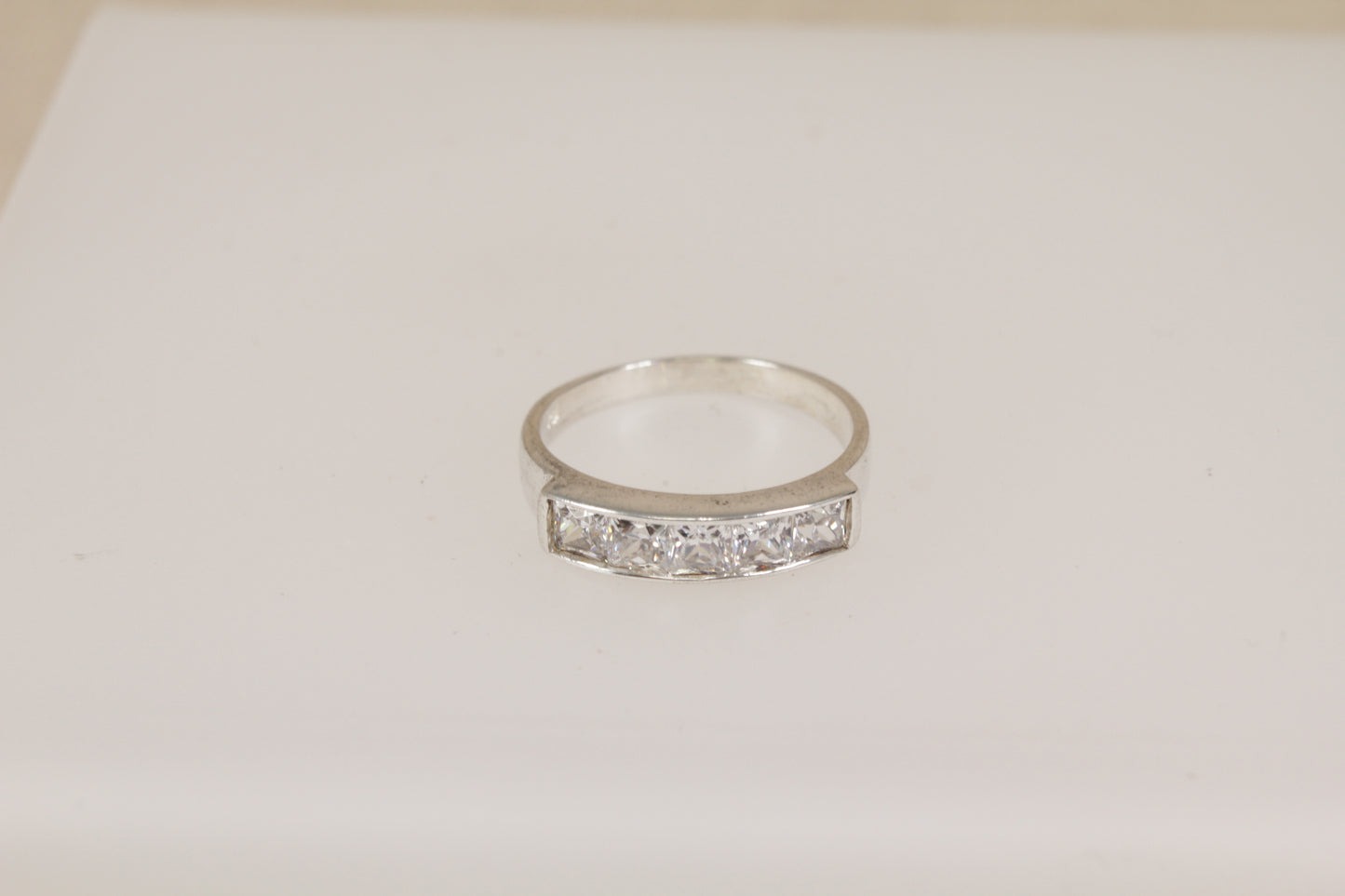 Silver ring with embedded diamond simulant crystal gemstones on a light beige background