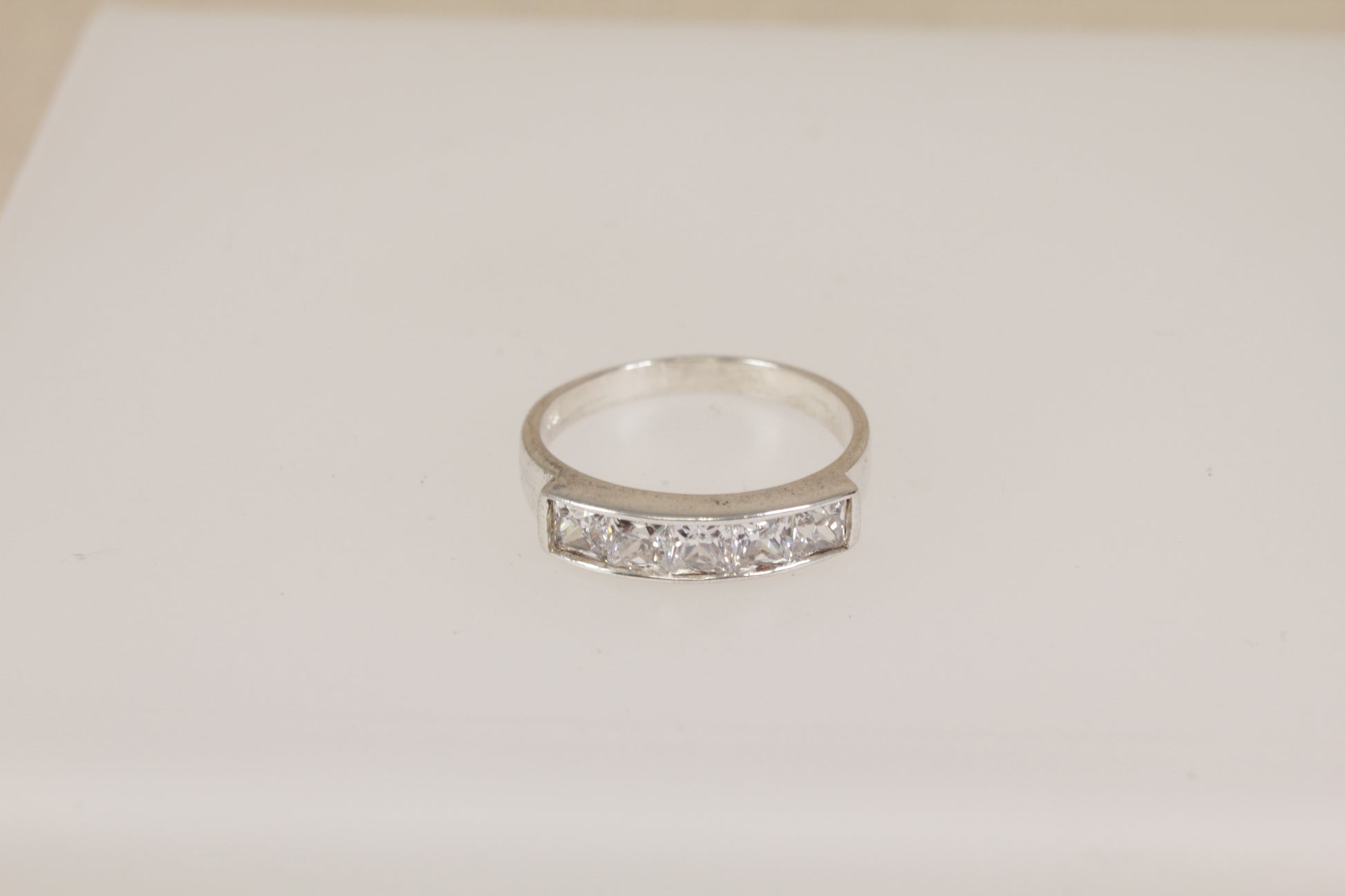 Silver ring with embedded diamond simulant crystal gemstones on a light beige background