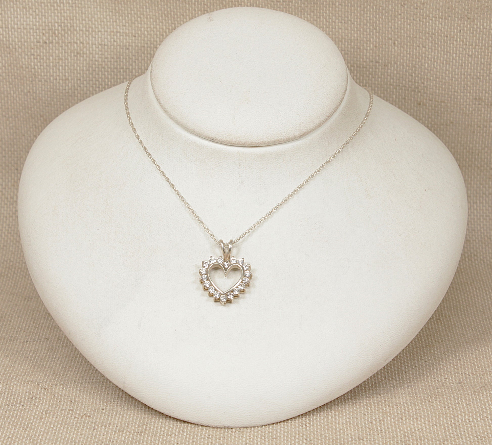 Silver heart-shaped pendant necklace on a white round stand with a beige background