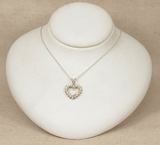 Silver heart-shaped pendant necklace on a white round stand with a beige background