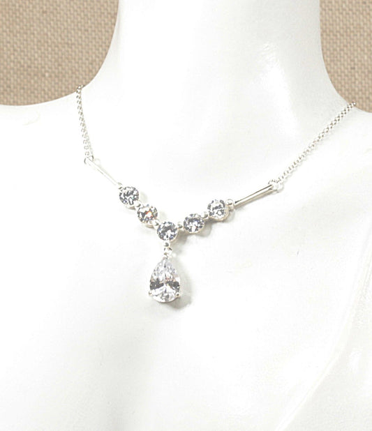 A silver necklace with a teardrop-shaped clear crystal pendant and smaller clear crystal beads along the chain, displayed on a white mannequin bust.