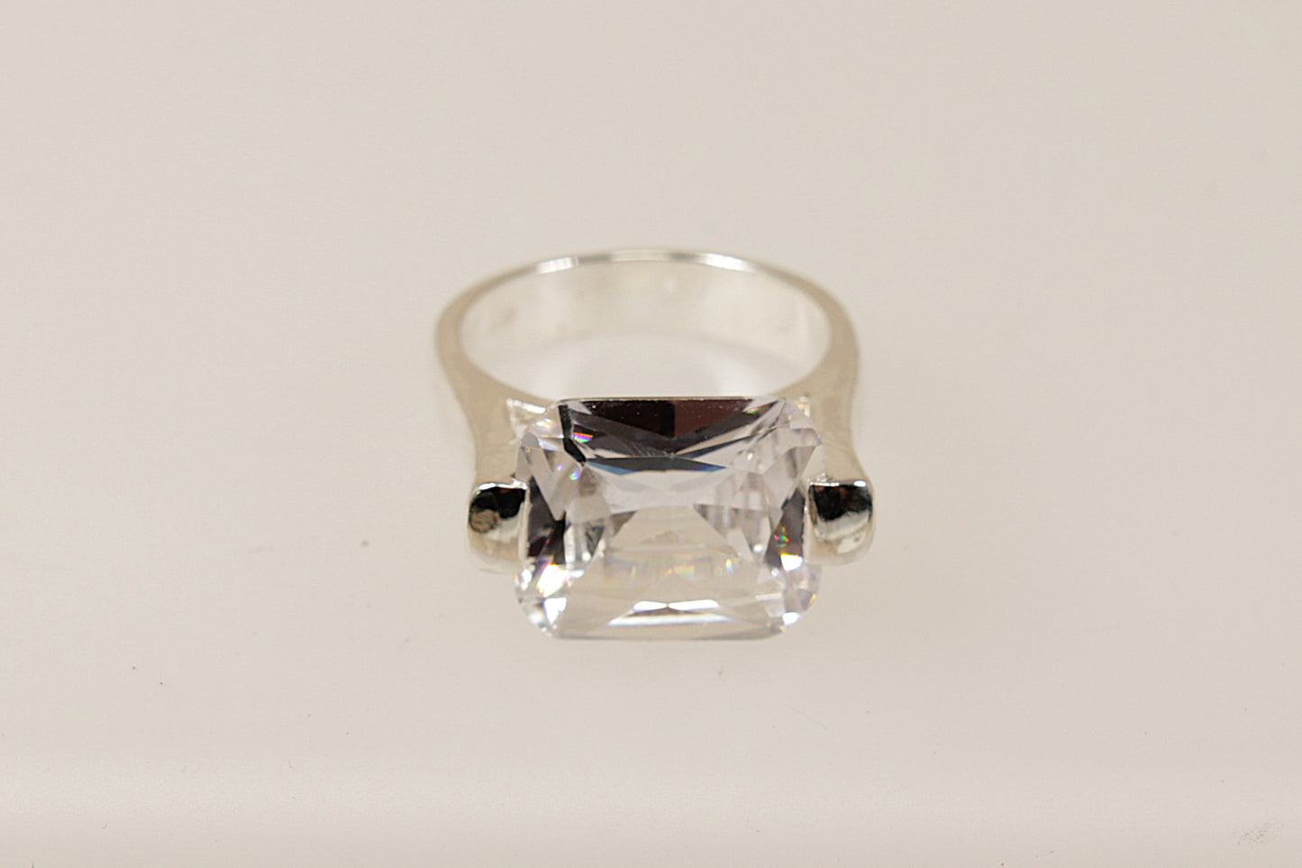 This silver CZ ring is a bold and striking piece, characterised by its substantial design and unique architectural setting.
The main feature is the large emerald cut Cubic Zirconia gemstone set in a cradle style mount, the stone is secured with 2 chunky claws that extend from the shoulders of the ring. The combination of the large CZ, heavy silver band, and innovative design makes this ring perfect for those who appreciate modern eye-catching statement jewellery. 

It is in excellent condition and inside t