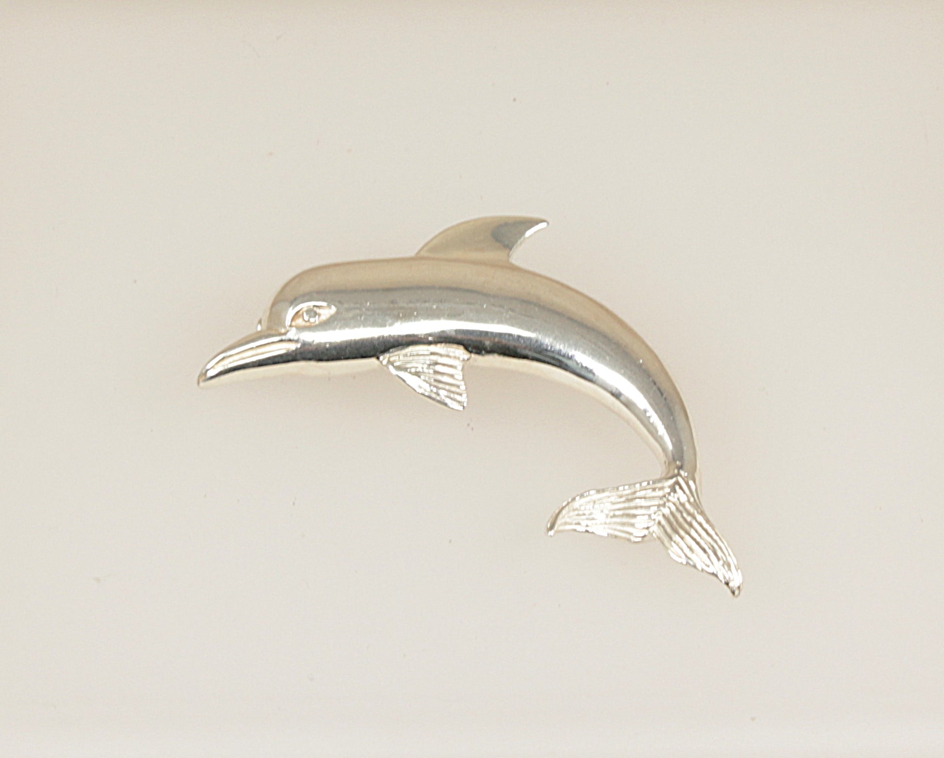 Silver dolphin figurine brooch on a light beige background