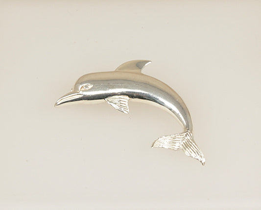 Silver dolphin figurine brooch on a light beige background