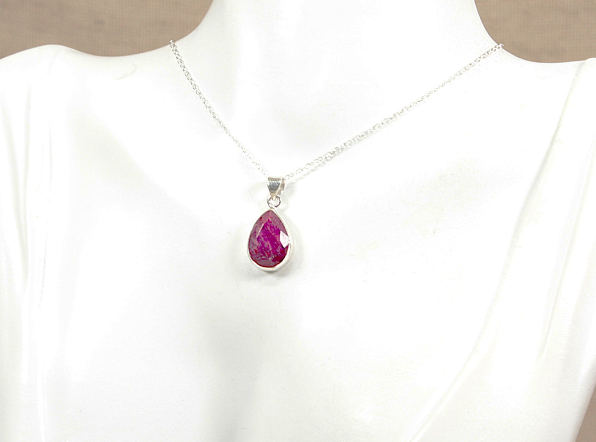 Silver necklace with a teardrop-shaped ruby pendant on a white mannequin against a beige background