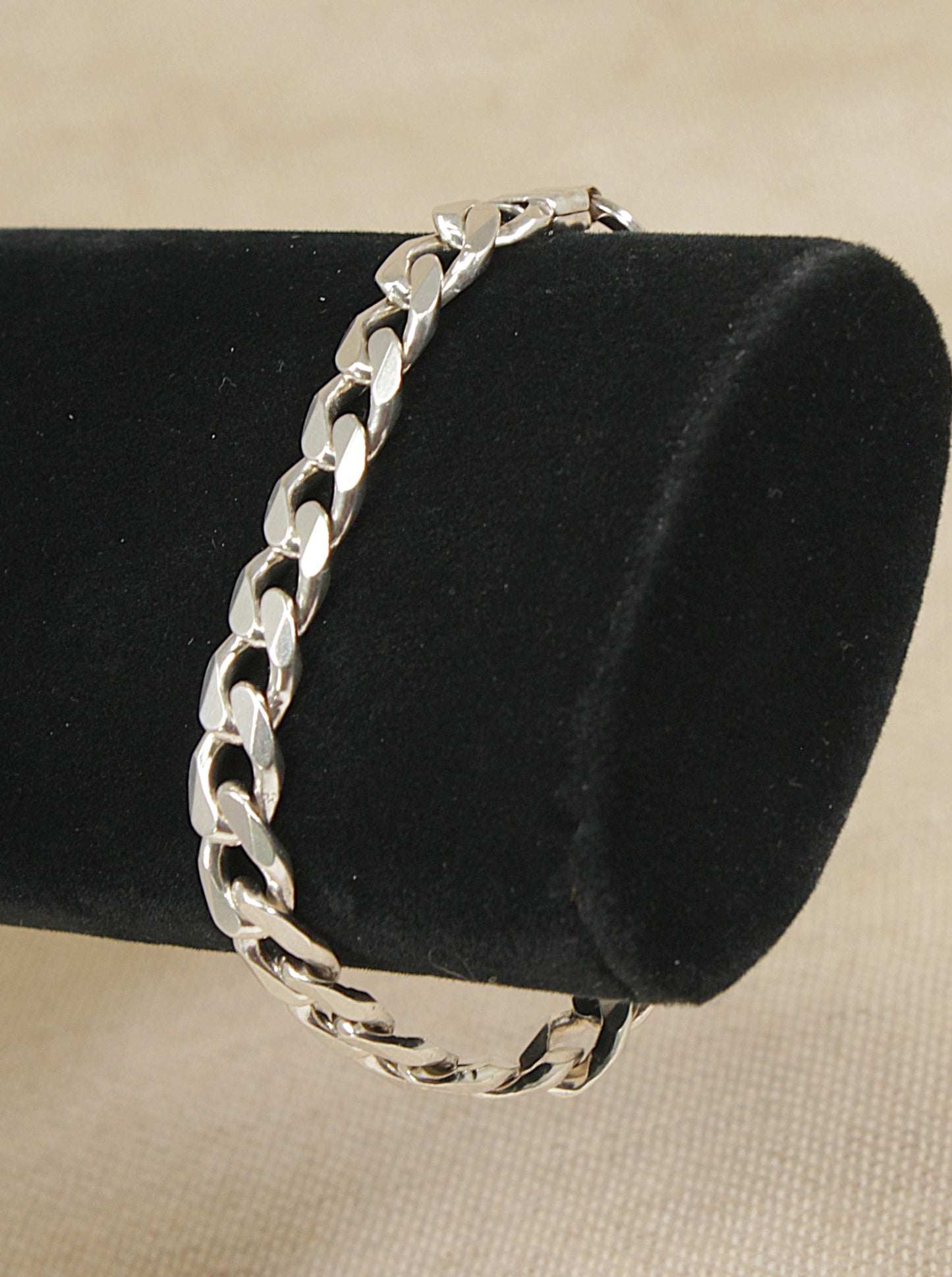 Sterling silver curb link bracelet on a black stand with a beige background