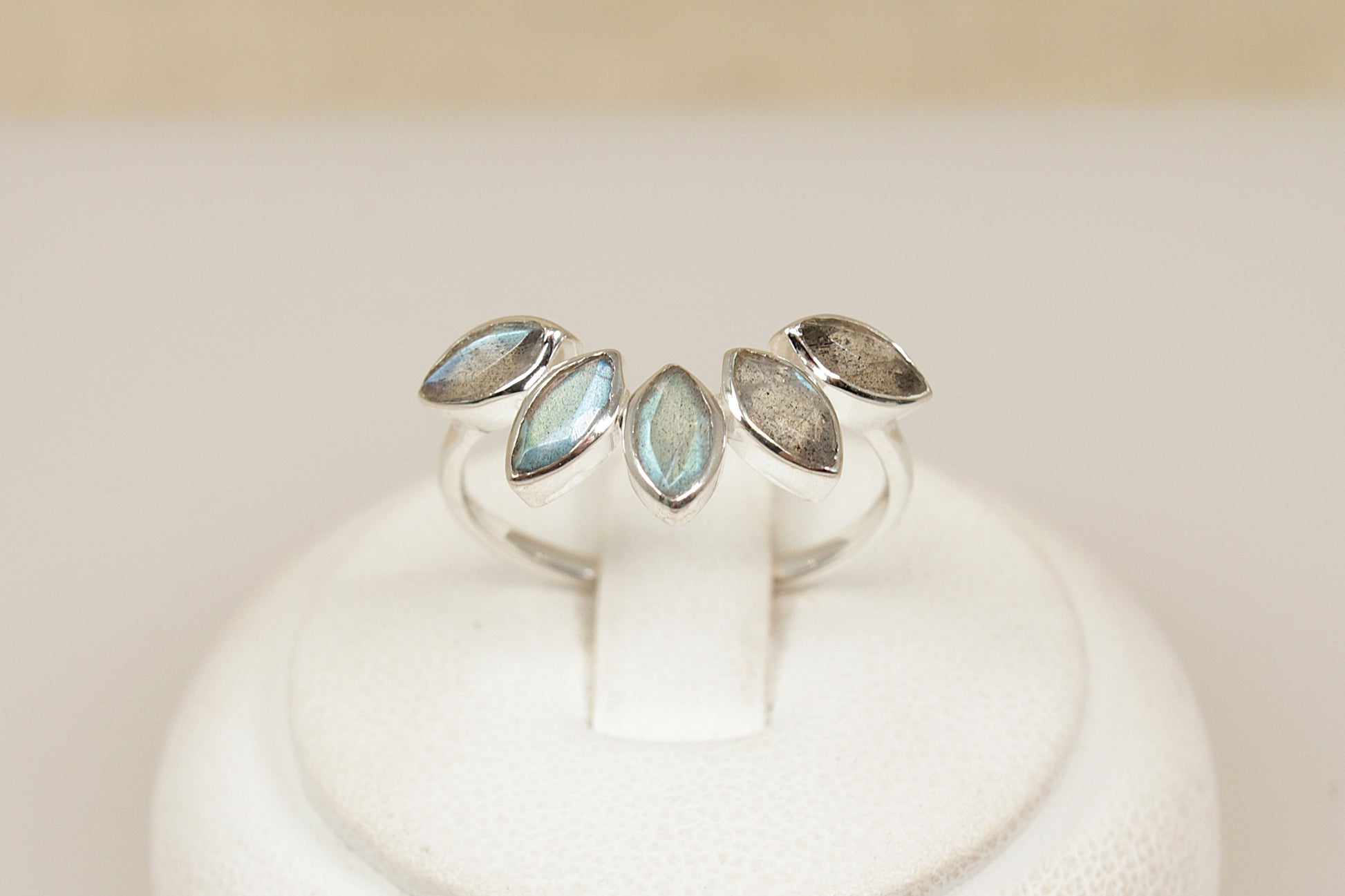 Silver ring with a half halo of labradorite gemstones on a white stand