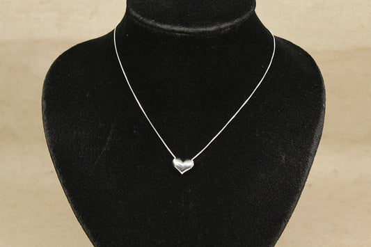Silver heart-shaped pendant on a black velvet mannequin against a beige background