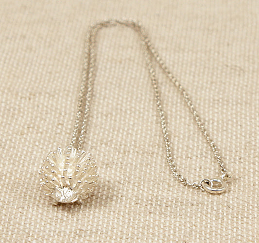 A sterling silver hedgehog pendant with a 'Prince of Wales' silver chain necklace laid out on a textured surface.